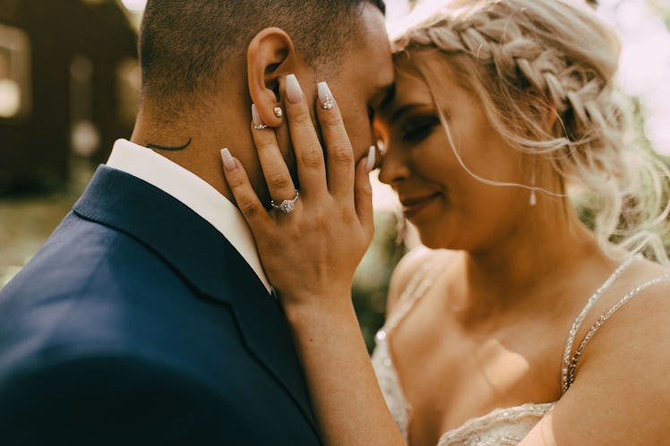 A couple embraces each other on their wedding day while dressed up and standing outside a cozy home.