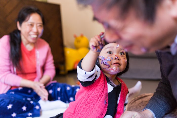 a young girl paints her grandfather's face