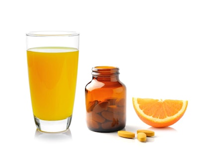 A glass of orange juice, a bottle of vitamin C pills and an orange 