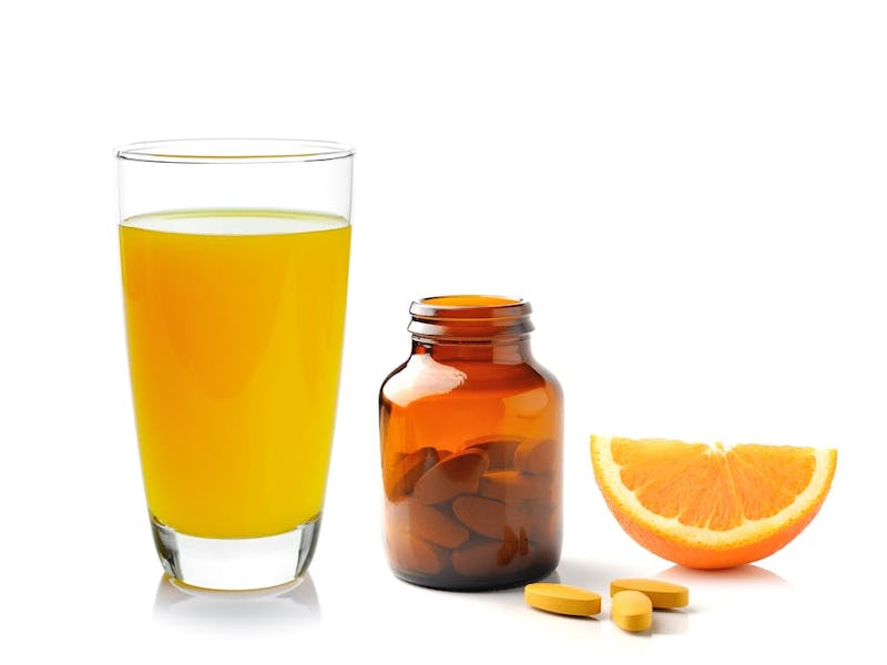 A glass of orange juice, a bottle of vitamin C pills and an orange