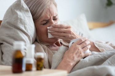 Ill middle-aged woman blowing her nose with a tissue while lying in bed
