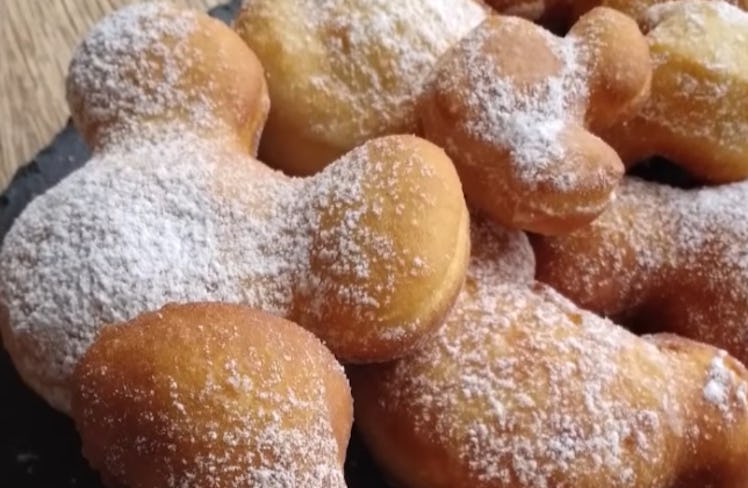 A stack of Disney Parks' Mickey Mouse-shaped beignets with powdered sugar on top sit on a plate.