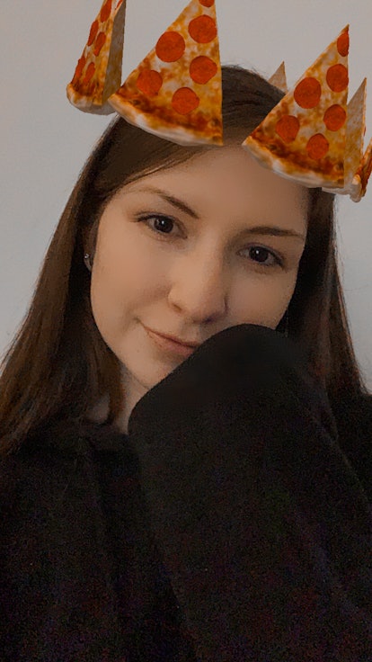 A young woman takes a selfie with an Instagram story filter that gives you a pizza crown.