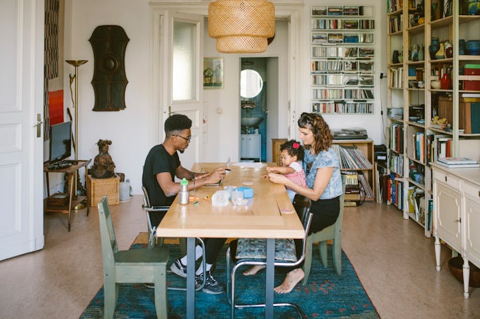 A mom works with child on laptop at home with husband
