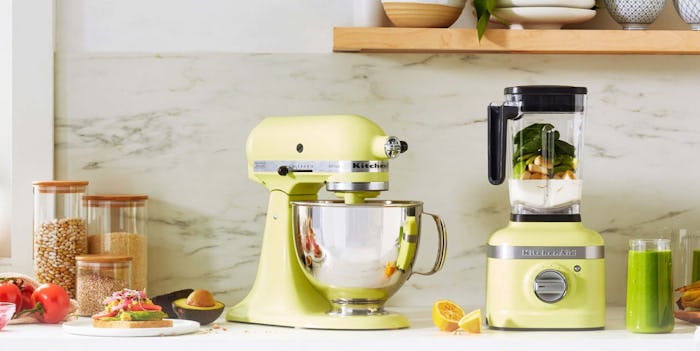 KitchenAid mixer and blender in "Kyoto Glow" on a counter top surrounded by nuts, veggies, fruits, a...