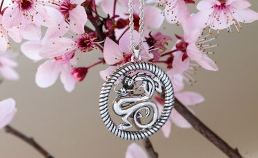 A Mushu necklace from the 'Mulan' RockLove Jewelry collection hangs from a magnolia flower branch. 