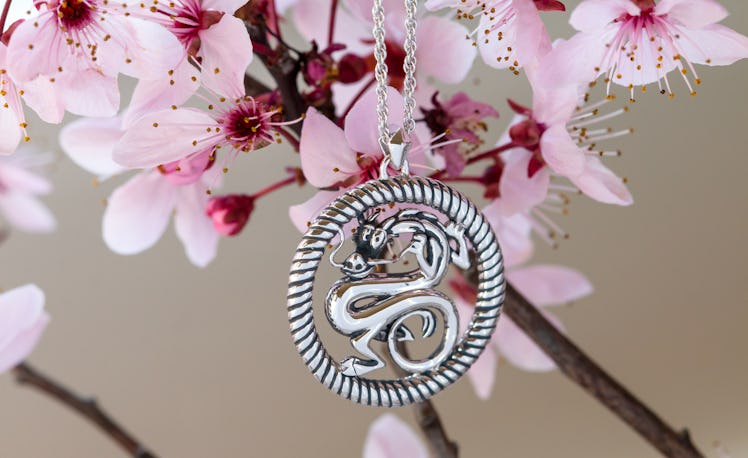 A Mushu necklace from the 'Mulan' RockLove Jewelry collection hangs from a magnolia flower branch.