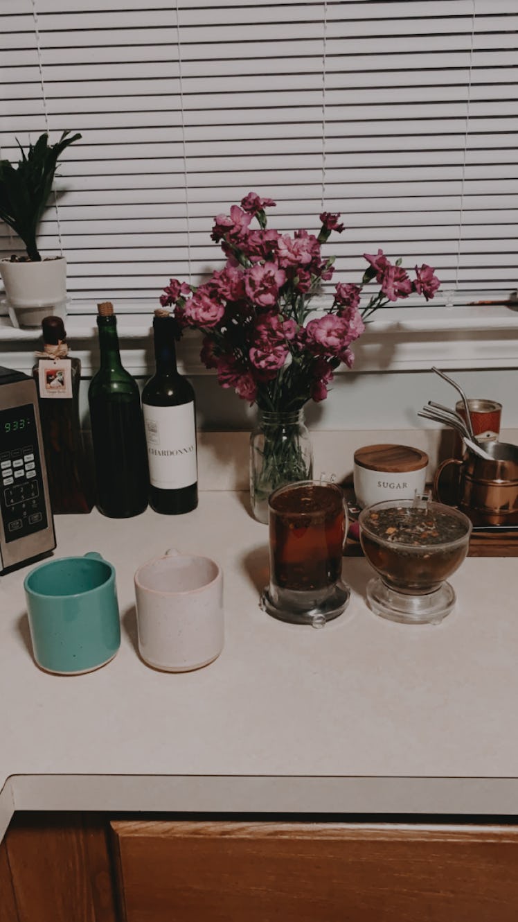 Colorful mugs sit on a kitchen counter while a couple brews fresh tea.