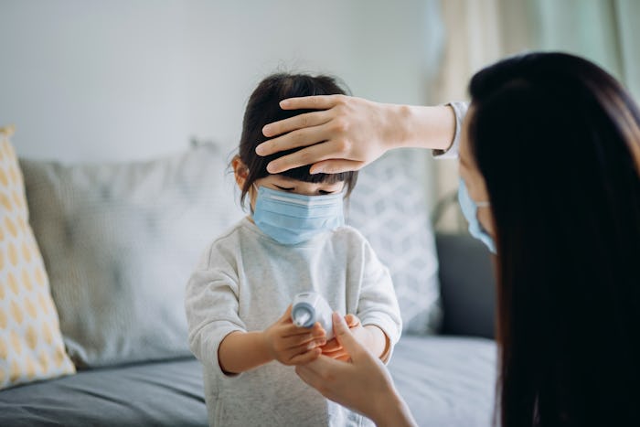 mom checking child's temperature with thermometer and hand on forehead