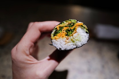 A woman's hand holds up a green salad hand roll at a restaurant in Mexico City.
