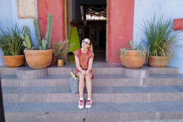 A woman dressed in a colorful dress and sneakers smiles while sitting on steps in Mexico City.