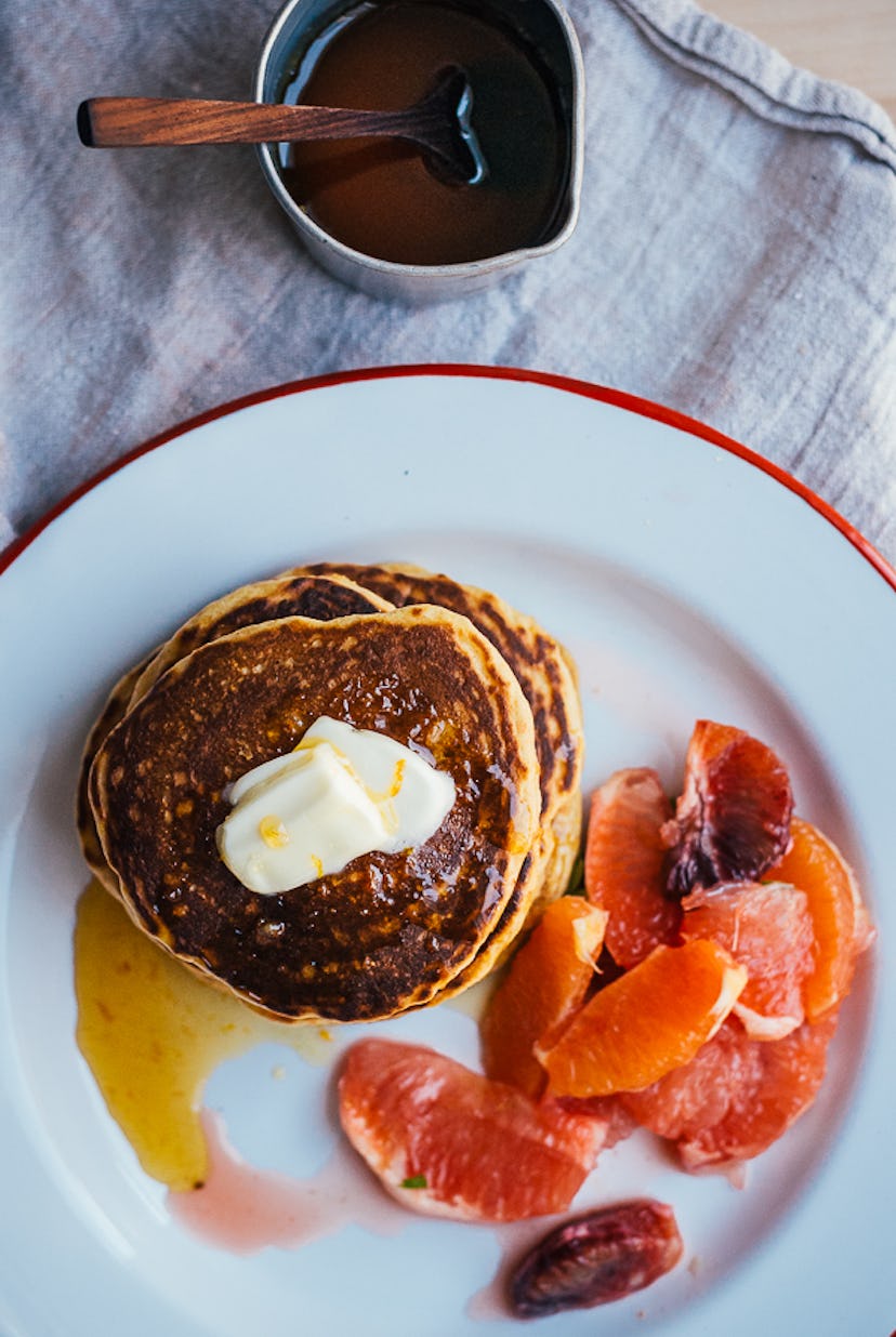 A picture of cornmeal pancakes with orange segments and honey syrup.