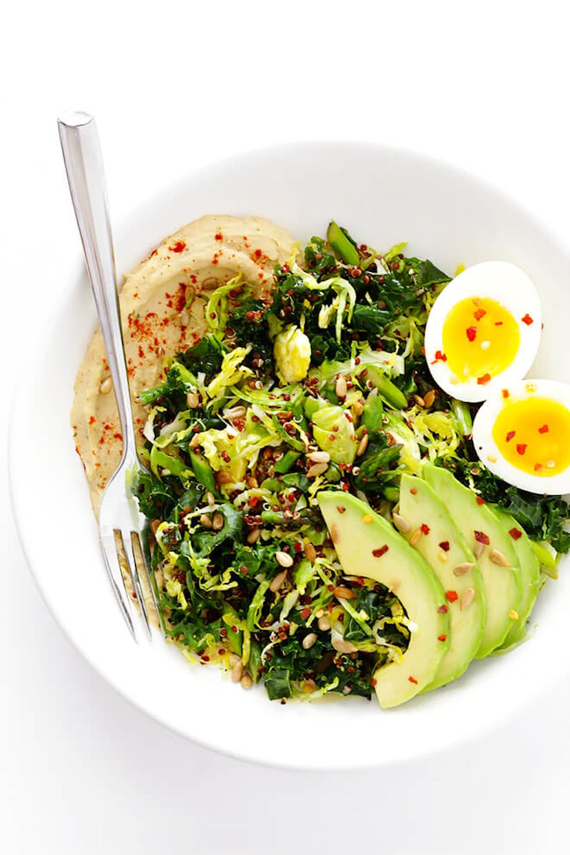 A bowl of greens, hummus, and hard boiled eggs. 