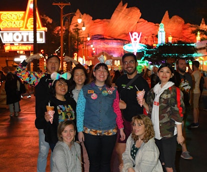 A group of friends stand together and pose in the middle of Cars Land at Disneyland.