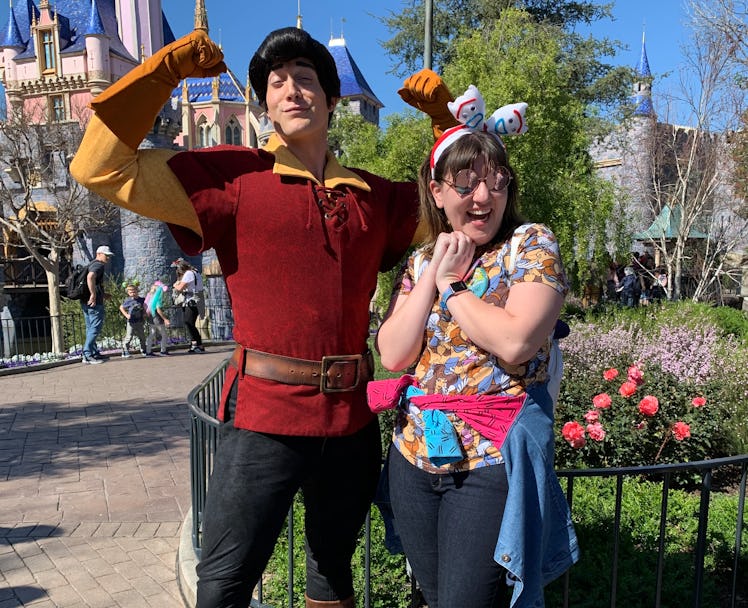A woman with a jacket tied around her wait poses with Gaston from 'Beauty and the Beast' in front of...