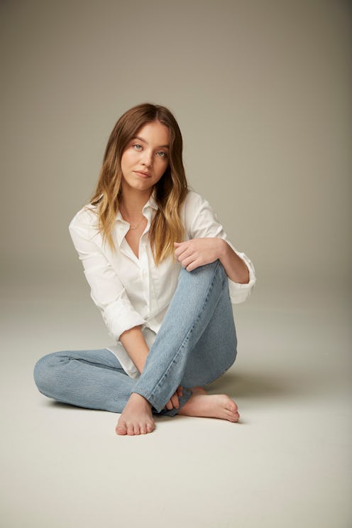 Sydney Sweeney sitting on the floor in a white shirt and light blue jeans