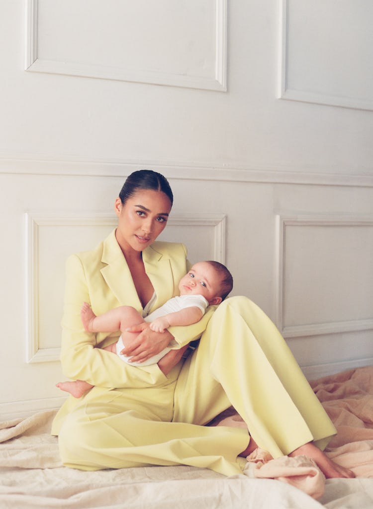 Shay Mitchell sitting and holding her baby while wearing Boss blazer, pants; Agnona bodysuit. Atlas ...