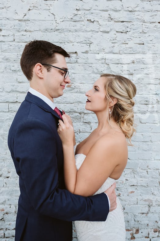 Rachel Varina and husband pose in front of white brick wall on wedding day