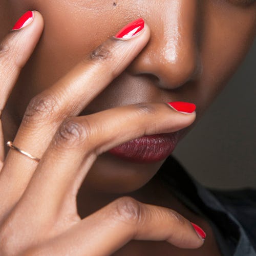 A lady holding her fingers with red manicure nails on her face