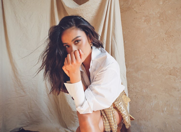 Shay Mitchell squatting and posing in Fendi top, sweater, shorts; Jenny Bird earrings.