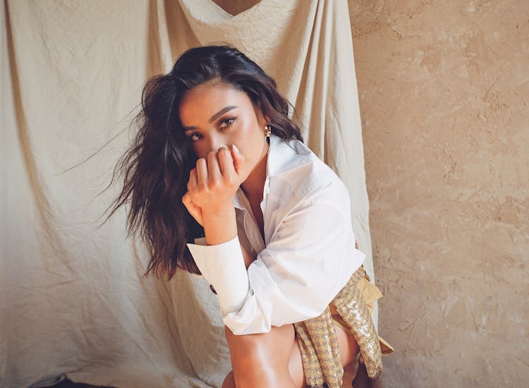 Shay Mitchell squatting and posing in Fendi top, sweater, shorts; Jenny Bird earrings.