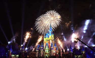 Fireworks light up the sky at night behind a lit up Cinderella castle at Disney World's Magic Kingdo...