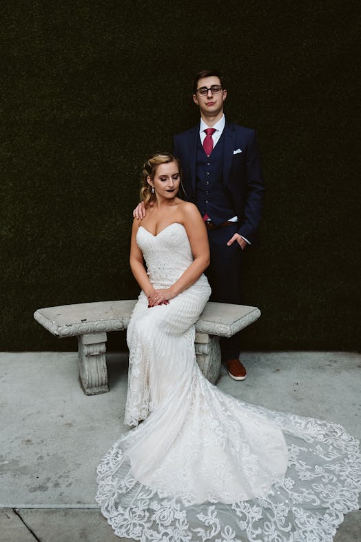 Rachel Varina in a Kitty Chen wedding gown poses on wedding day with husband in front of greenery wa...