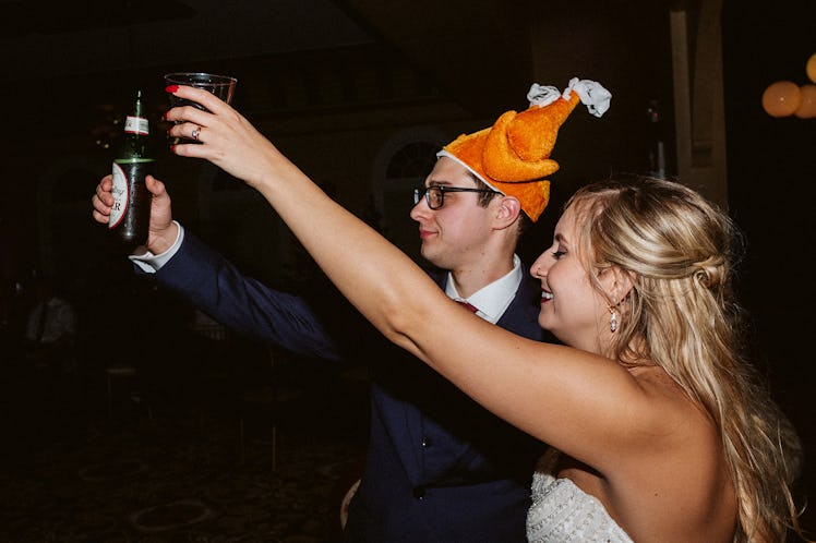 Rachel Varina and husband in turkey hat raise glasses for cheers at wedding reception