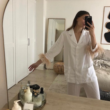 A woman wearing white silk pajamas with feathers on the sleeves to work from home