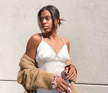 A girl posing in a white dress while holding a brown sweater