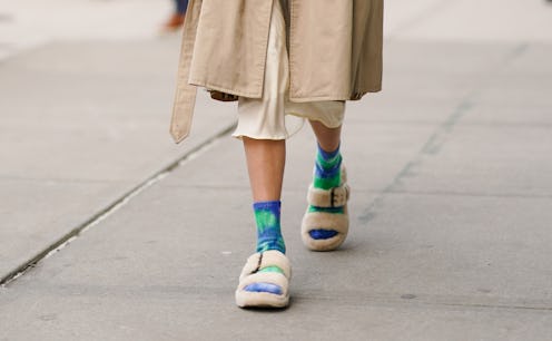 A woman walking in a white skirt, beige coat, blue-green socks and white shoes