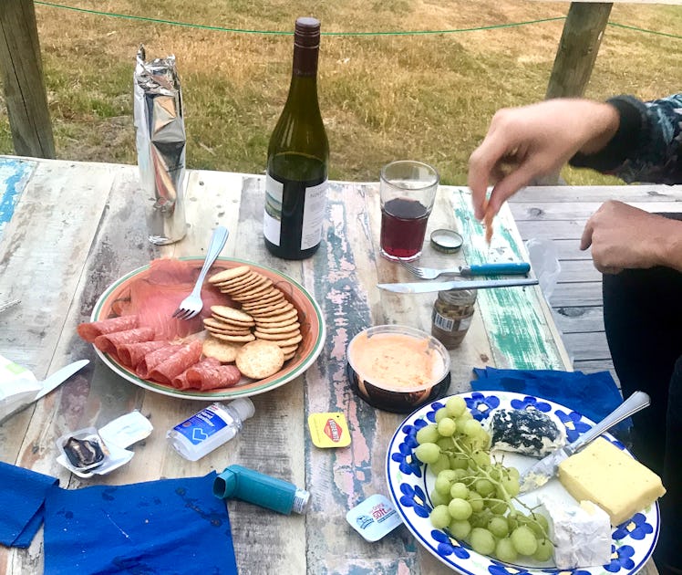 A picnic table has plates of meats, cheeses, and fruit on it.