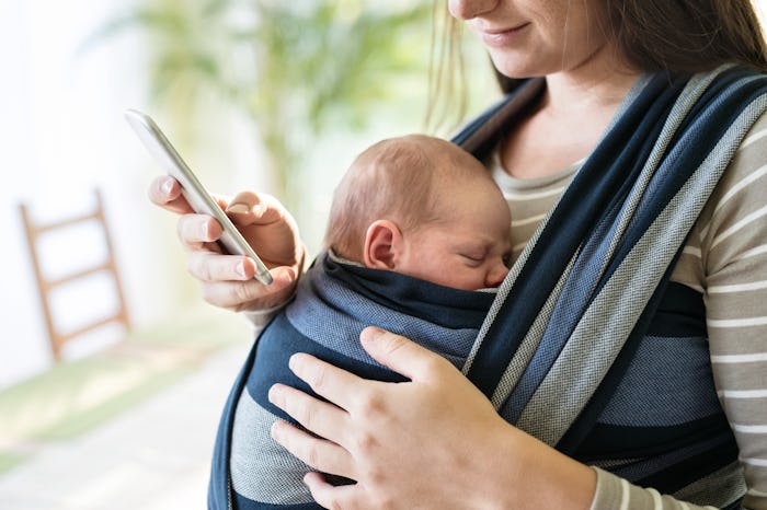 Unrecognizable mother with her son in sling and smartphone