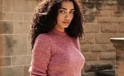 A brunette curly-haired woman in a pink spring sweater