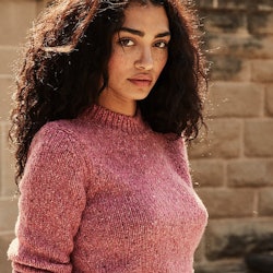 A brunette curly-haired woman in a pink spring sweater