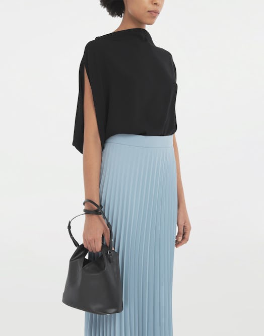 A model in a light blue pleated skirt with a black sweater holding a black MM6 Maison Margiela's  Ja...