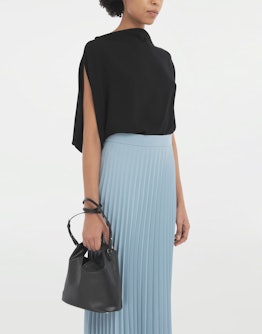 A model in a light blue pleated skirt with a black sweater holding a black MM6 Maison Margiela's  Ja...