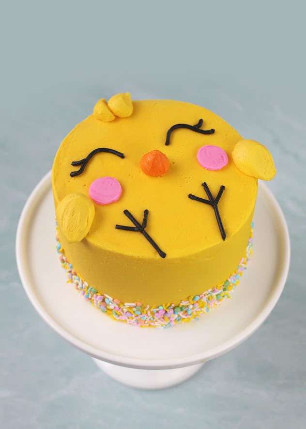 Cake decorated to look like a cartoon chick on a white cake stand