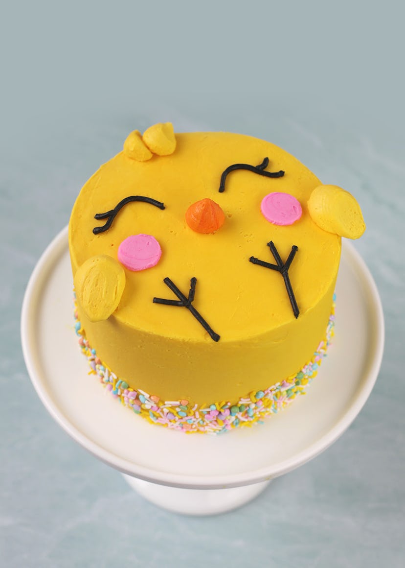Cake decorated to look like a cartoon chick on a white cake stand