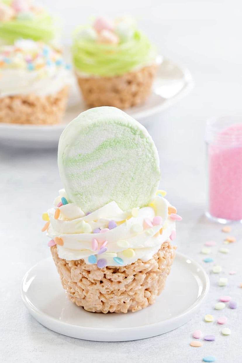 Cupcake made from rice krispie treats, topped with frosting and a marshmallow egg on a white plate w...