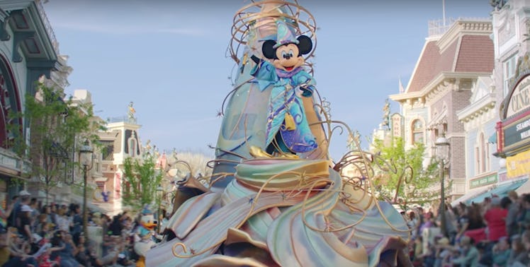 Mickey Mouse stands on top of a float in a Disney parade going down Main Street.