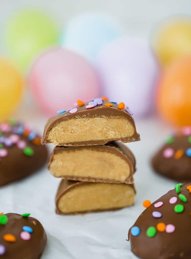 Three peanut butter and chocolate eggs cut in half and stacked with others (out of focus) surroundin...