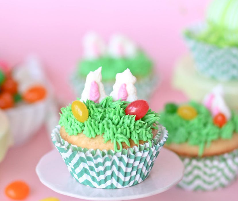 Cupcake on a plate decorated with icing "grass", jelly beans, and bunny ears popping up