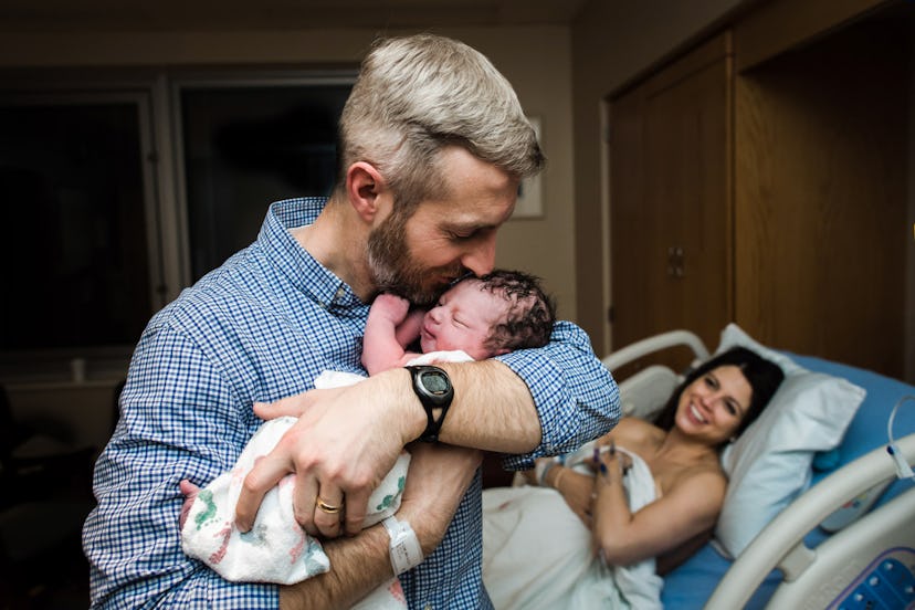 Smiling dad kisses newborn baby while holding for the first time