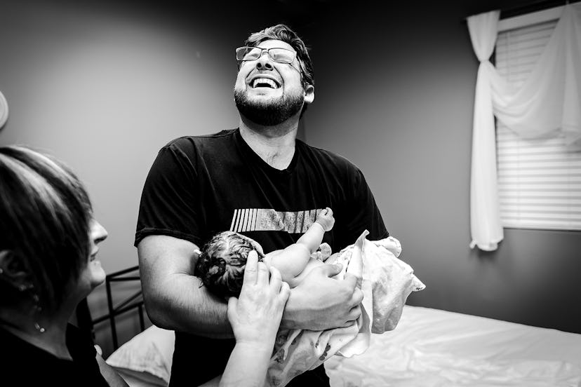 Dad smiles while holding newborn baby in swaddle