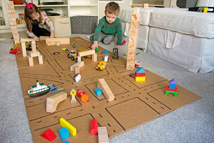 Children play with block cars on a cardboard traffic system.