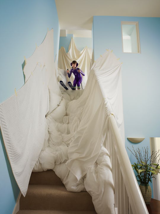 A child stands at top of a staircase with skis on their feet.