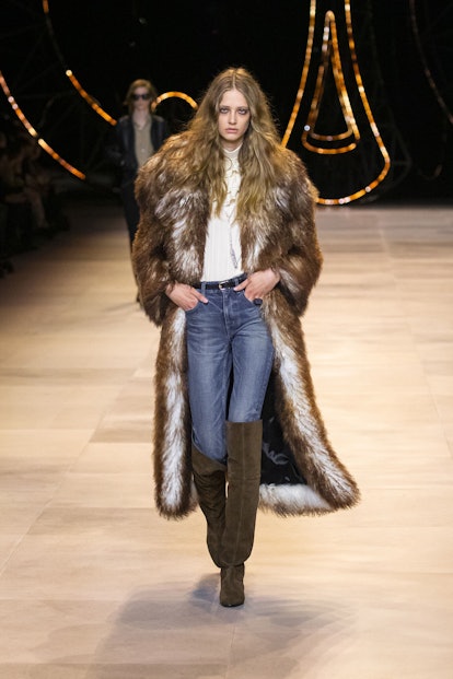A model wearing jeans, a white shirt, brown over the knee boots and a matching fur coat by Celine