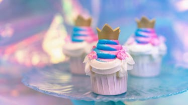 A pink and blue cupcake with a gold crown sits on a cupcake tray.