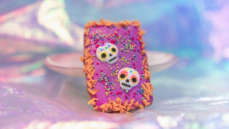 A colorful Dia de los Muertos hand pie with sugar skulls leans against a plate and is served at Disn...
